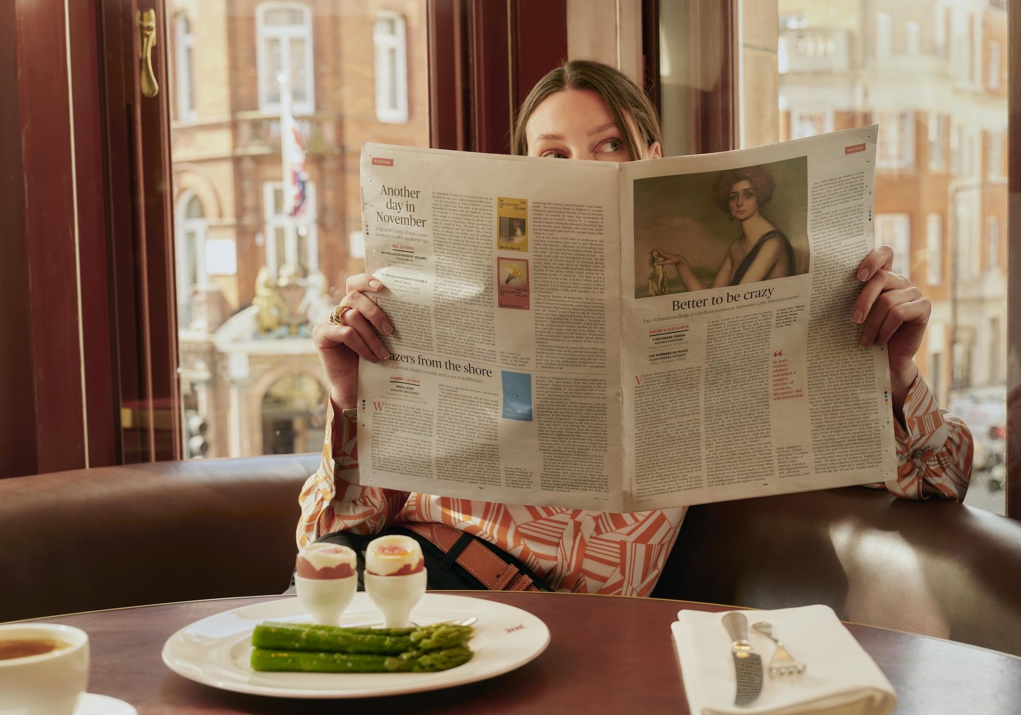 A lady reading a newspaper during breakfast at Mount St. Restaurant, in front of a plate of asparagus and boiled eggs.
