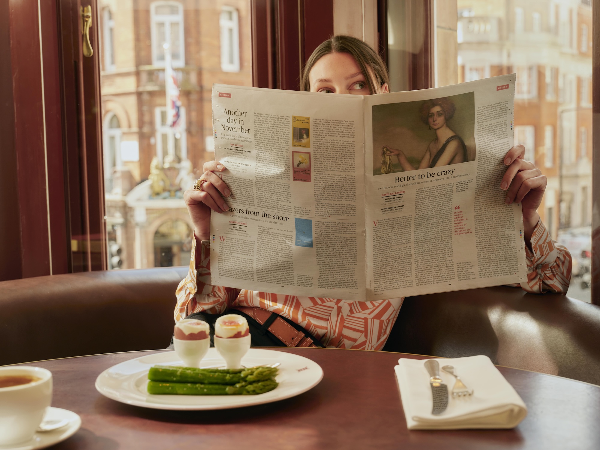 A lady reading a newspaper during breakfast at Mount St. Restaurant, in front of a plate of asparagus and boiled eggs.
