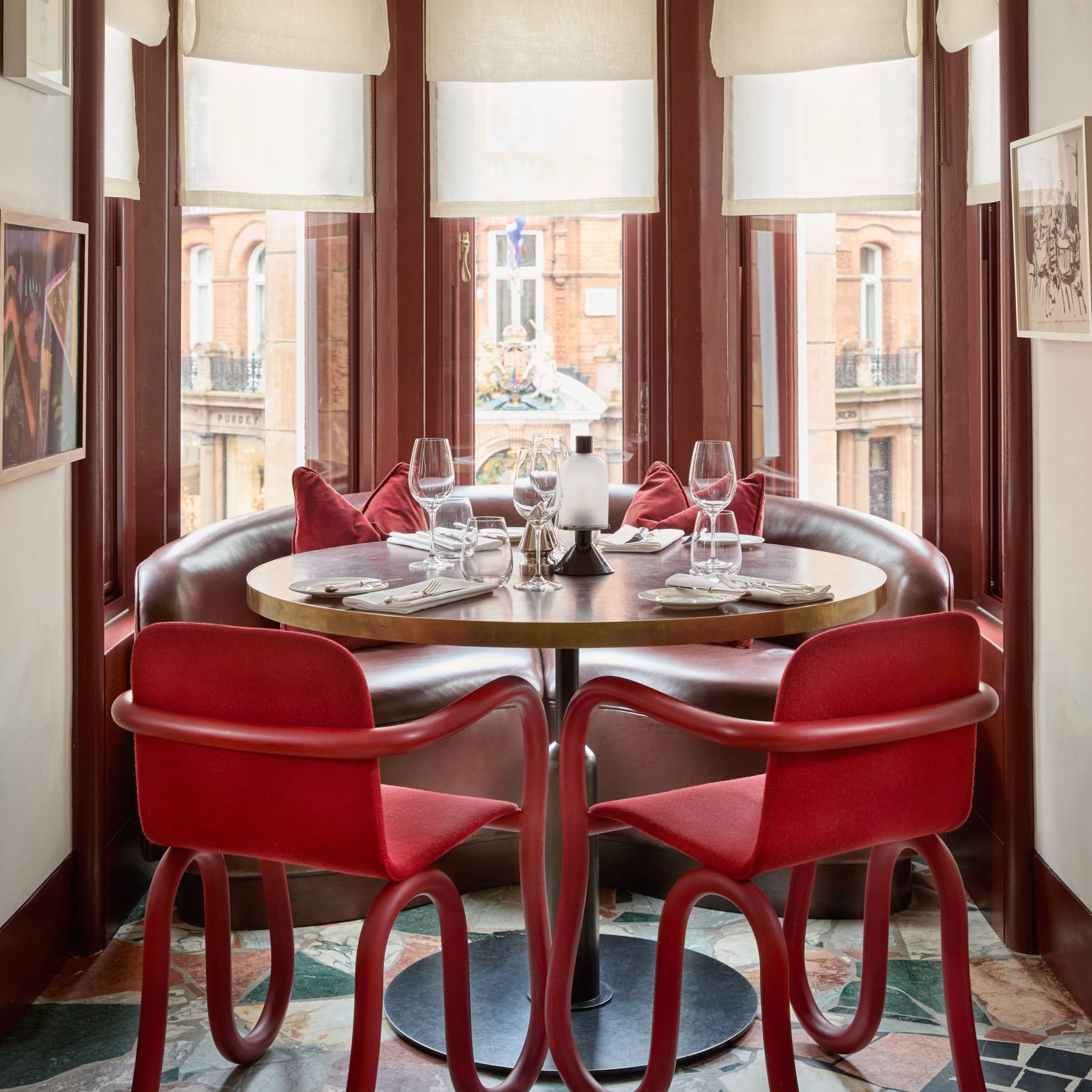A round dining table with four red chairs around it in Mount St. Restaurant with multiple artworks and windows in the background