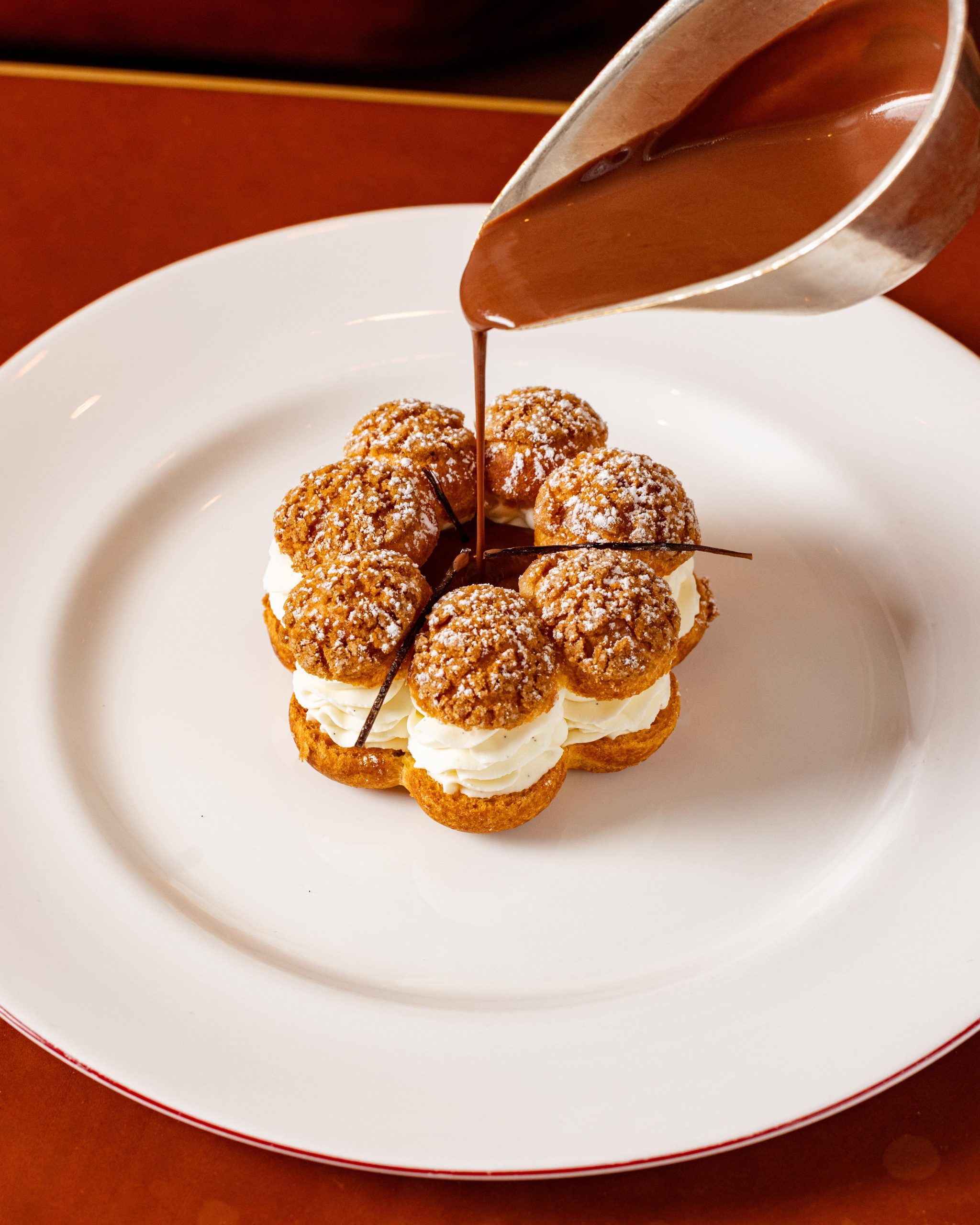 Choux bun, Guernsey vanilla cream, with hot chocolate sauce being poured
