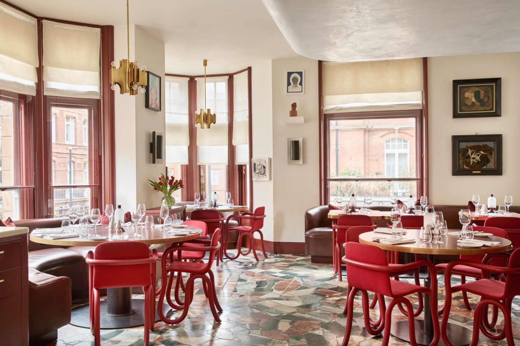 The dining area in Mount St. Restaurant, featuring tables with burgundy leather tops, with red chairs around them. The walls showcase various artworks.