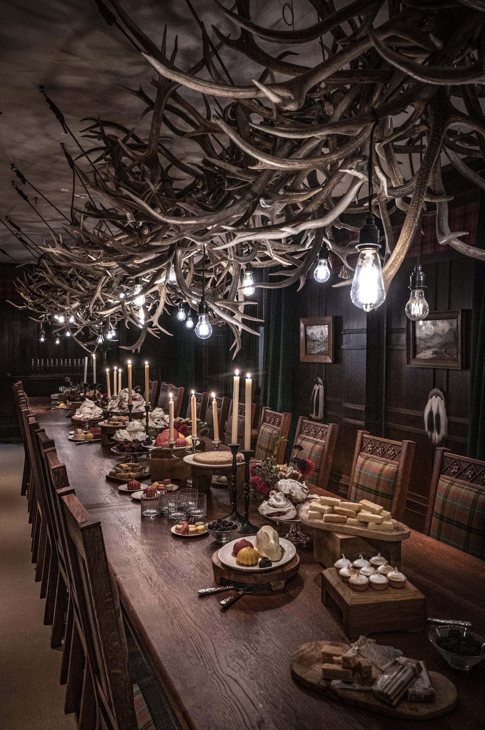 The 26-seat hand-carved table in The Scottish Room with oak chairs upholstered in green and red tartan. A banquet is laid out on the table, with candles alight.